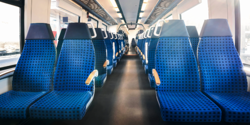 Interior view of a modern commuter train with blue seats and bright daylight shining through the windows
