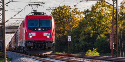 Red regional train travelling on rails through a rural area