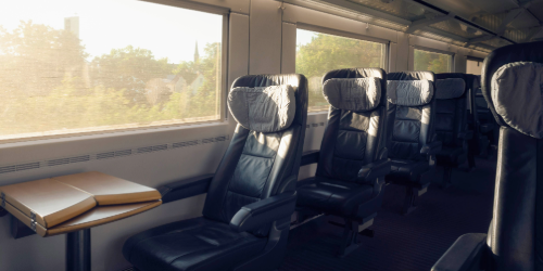 Interior view of a comfortable passenger train car with black leather seats and a table, with sunny daylight streaming through the windows