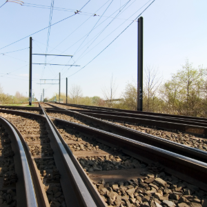 Close-up of railway tracks with a switch, surrounded by power lines and a green landscape